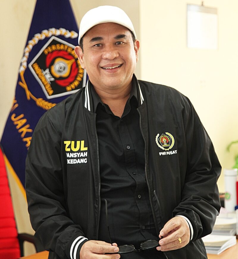 Sekjen PWI Pusat terlihat berpose di ruang kerjanya, mengenakan jaket resmi PWI Pusat. Momen ini diambil saat ia menjelaskan tiga Surat Edaran terbaru terkait rangkap jabatan, perpanjangan KTA, dan donasi kemanusiaan untuk bencana banjir Sumatera.